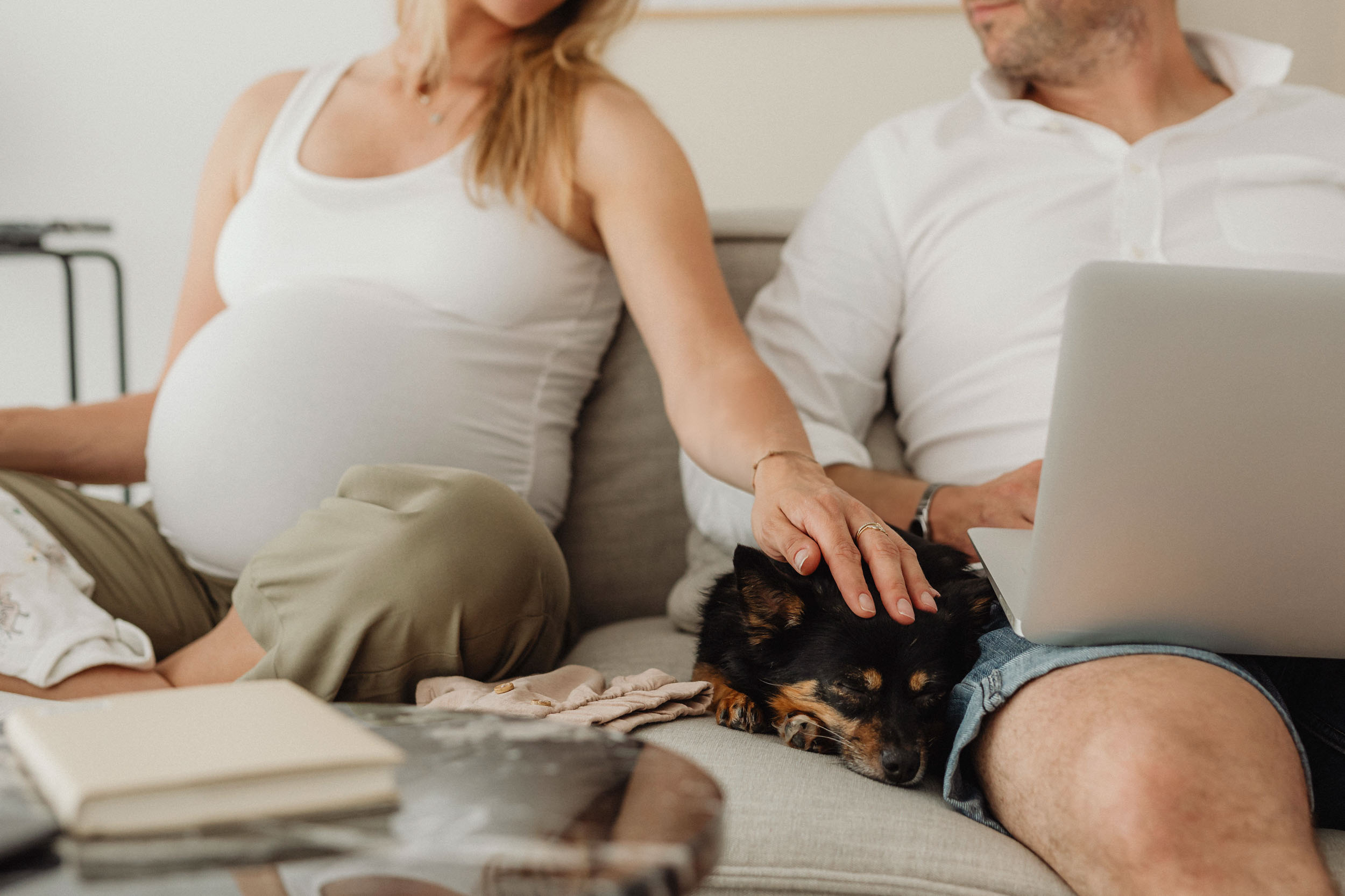 A man and pregnant woman relax on a couch with a dog enjoying each other s company in a cozy living room