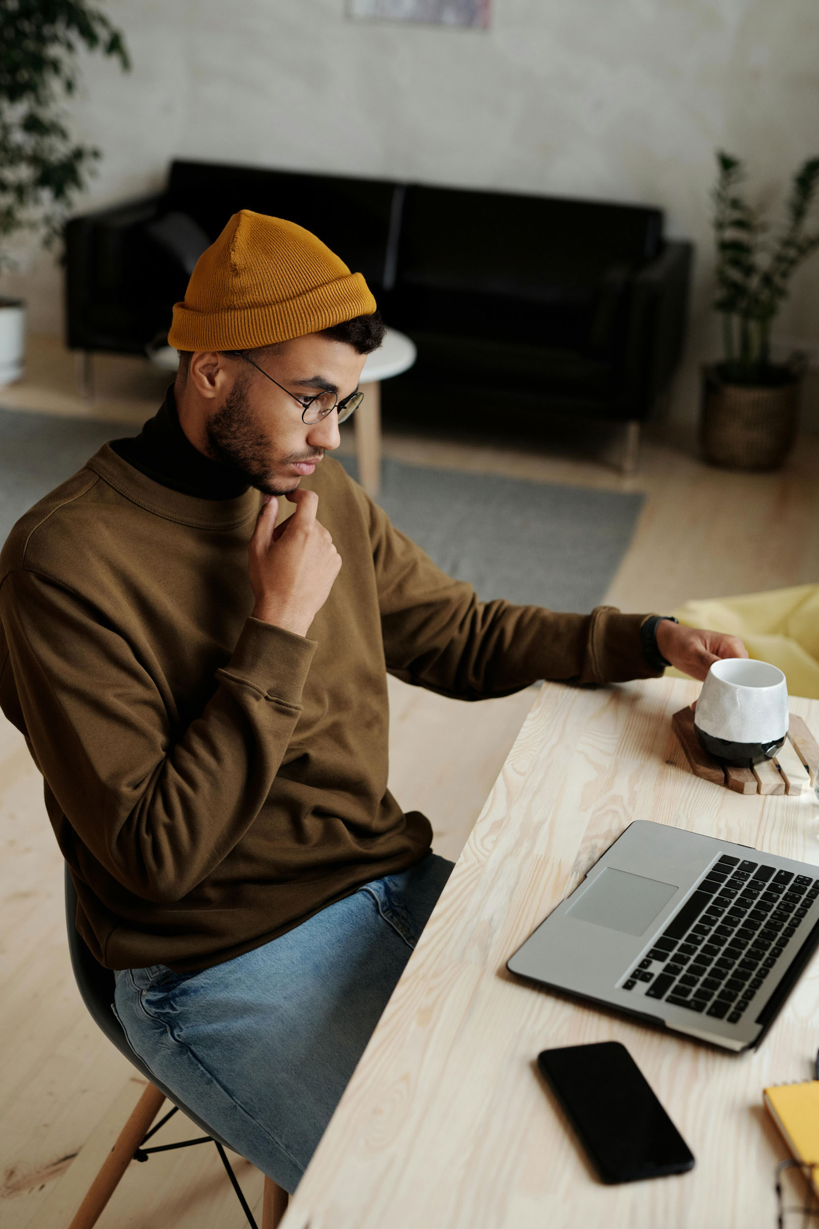 A man wearing a beanie sits at a desk focused on his laptop 1