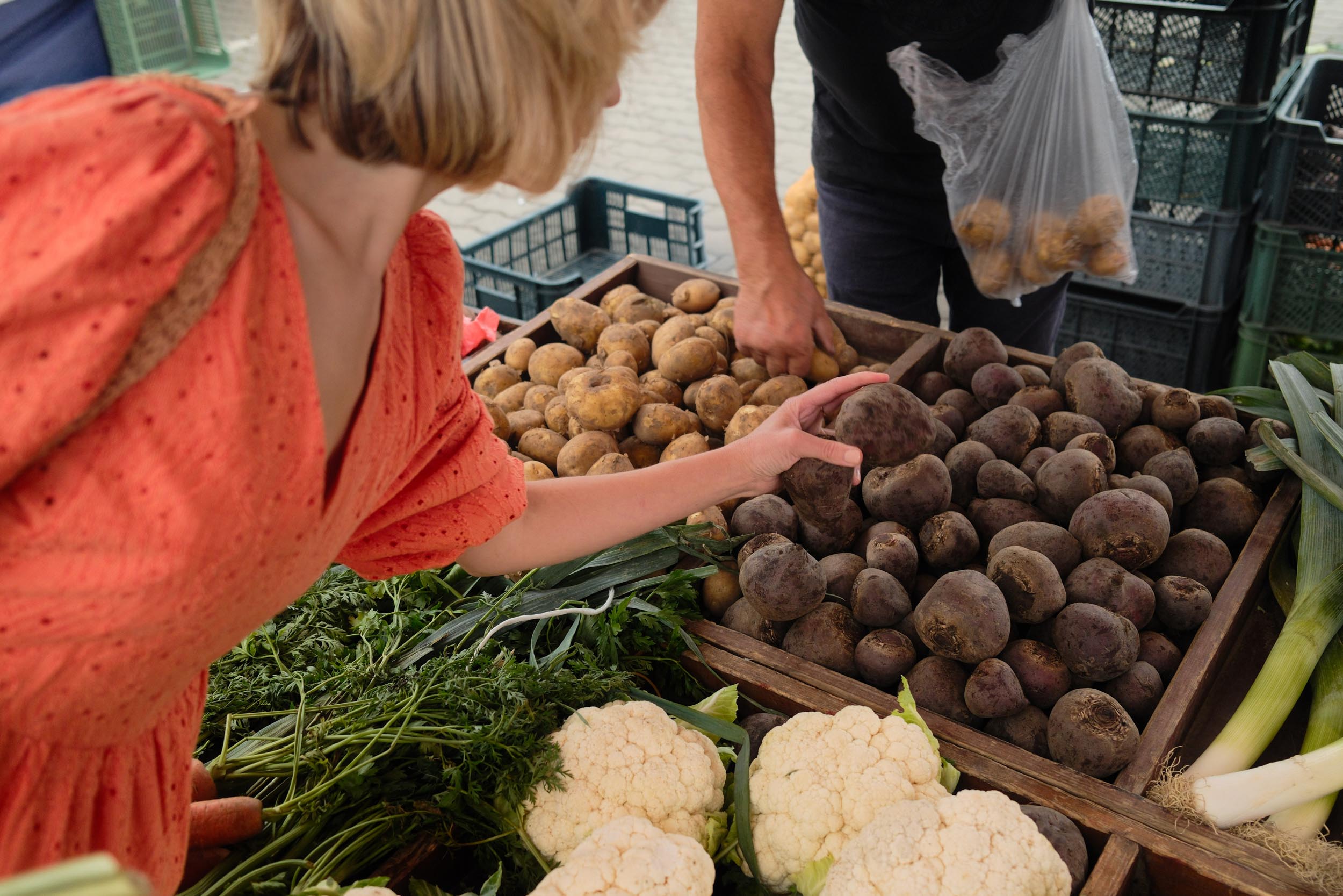 A woman examines fresh vegetables at a vibrant farmers market surrounded by colorful produce and other shoppers 1