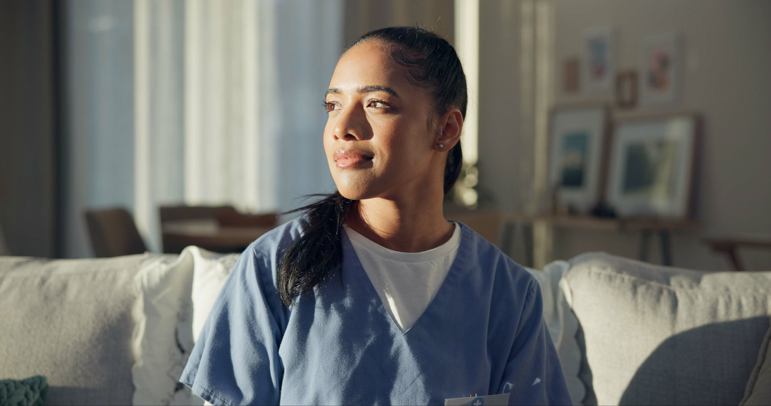 A woman in scrubs relaxes on a couch looking comfortable and at ease 1