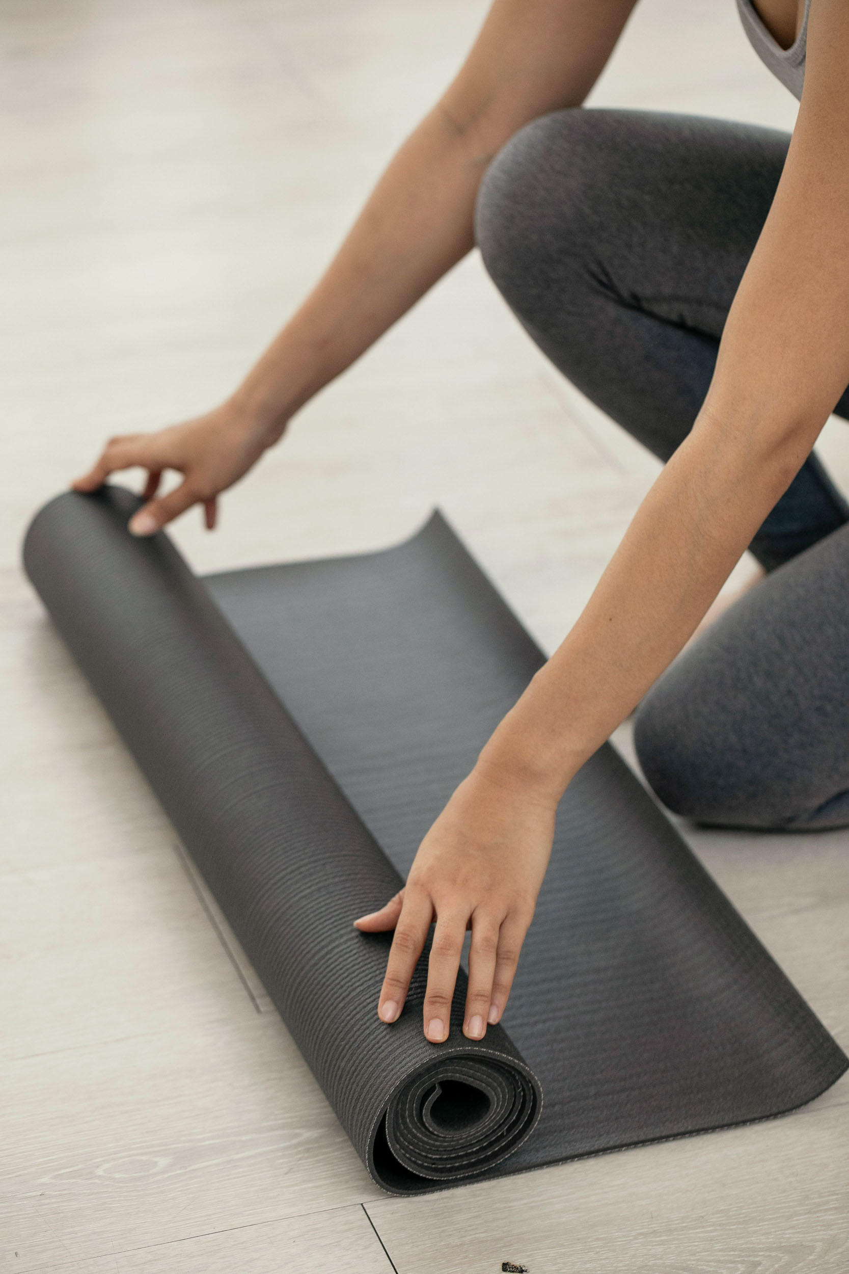 A woman kneels on a yoga mat preparing for her practice on a wooden floor 1