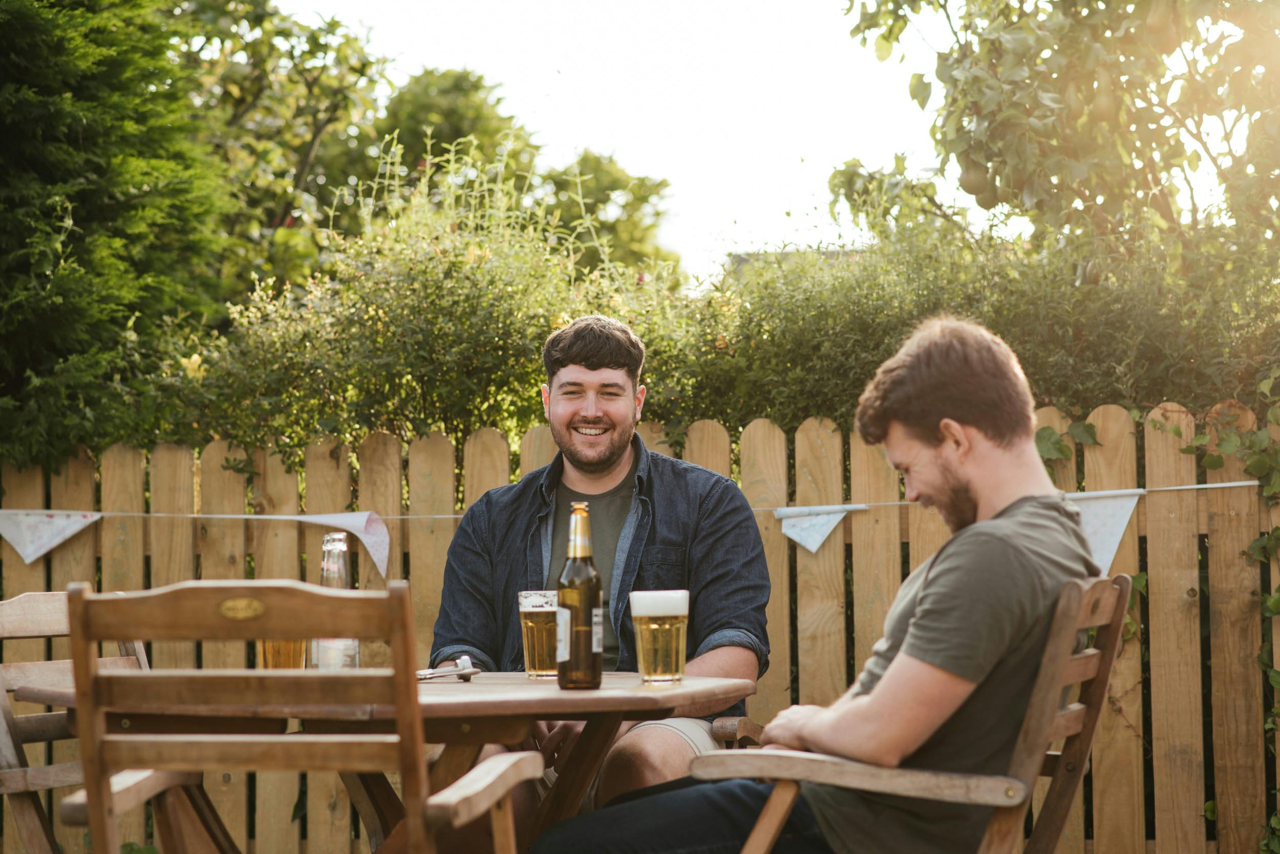 Two men sitting at a table enjoying drinks from beer bottles and chatting casually 1